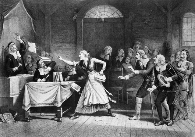 Drawing of a woman pointing a finger at a judge while a crowd of men watches on during a witch trial.
