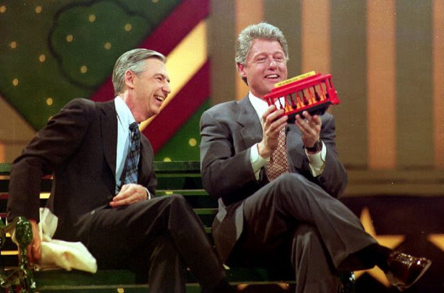 Mr. Rogers and Bill Clinton laughing together while looking at a toy tram.
