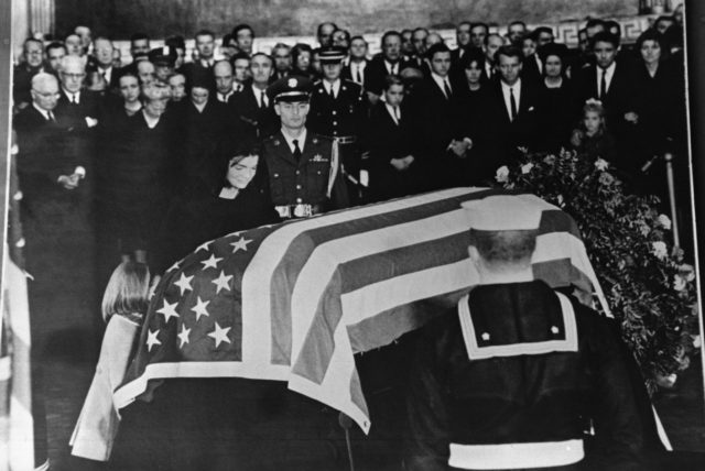 A group gathered around a casket with an American flag over it