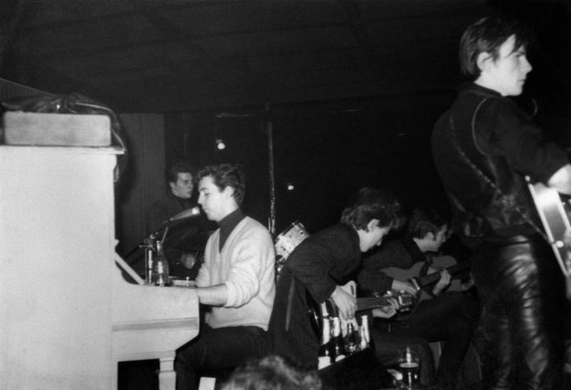 Pete Best, Paul McCartney, George Harrison, John Lennon, and Stuart Sutcliffe performing a musical number on stage.