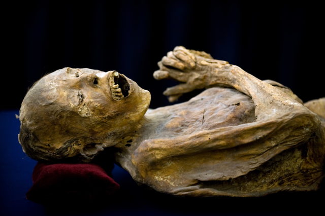 A mummy laying with hand at chest and mouth open
