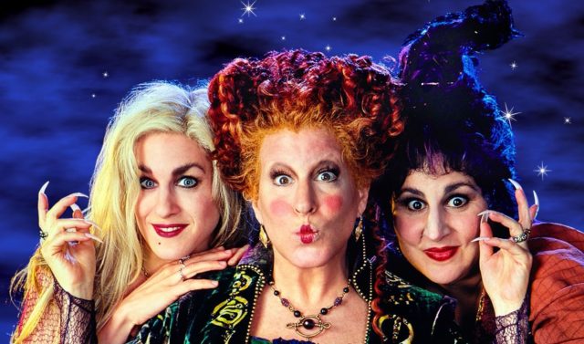 Bette Midler, Kathy Najimy, and Sarah Jessica Parker dressed as their 'Hocus Pocus' characters leaning their heads close together while looking at the camera.