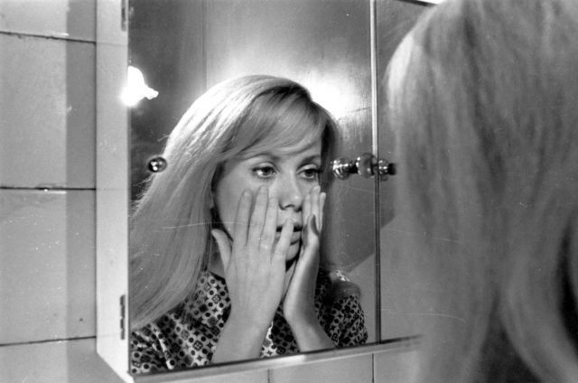 A woman looks at herself in the mirror with hands to her cheeks