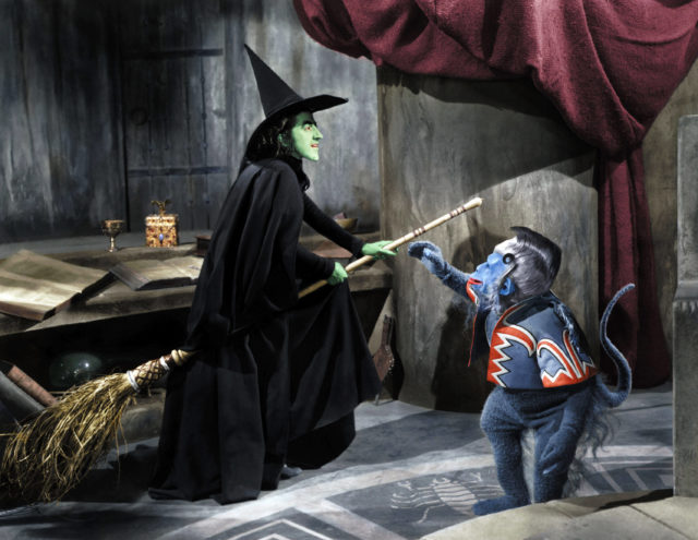 Wicked Witch of the West on a flying broom talking to one of her evil monkeys in 'The Wizard of Oz.'