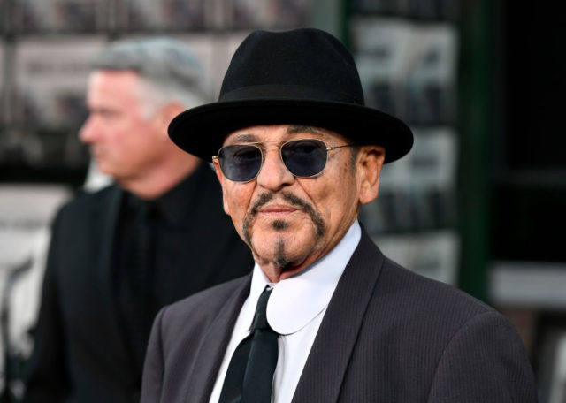 Joe Pesci in a black suit, tie, and white collared shirt with sunglasses and a black hat.