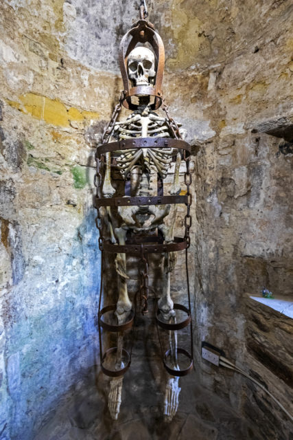 A skeleton in a cage hung in a cave