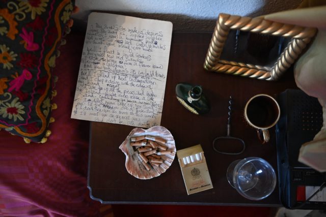 A handwritten not sitting on a table beside cigarettes, cigarette butts, a cup, and a photo frame