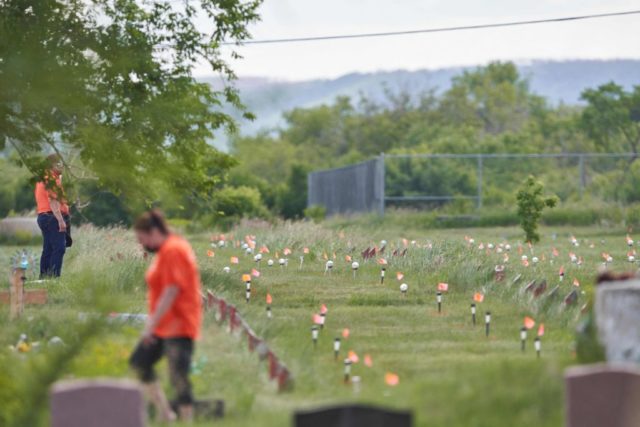 Volunteers walk among the hundreds of flags marking the unmarked graves of Canadian residential school children