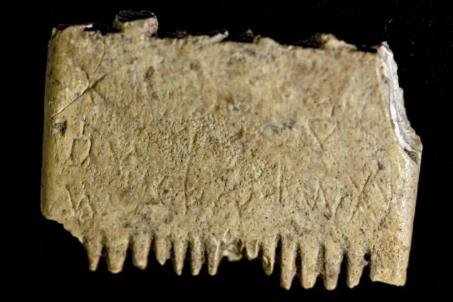 Ivory comb with missing teeth and faint inscription carved on the body.