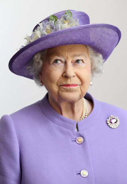 Portrait of Queen Elizabeth II in a purple jacket and matching hat with flowers.