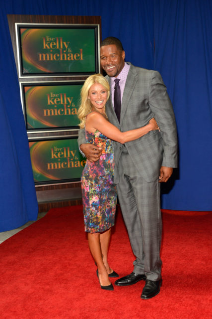Kelly Ripa hugging Michael Strahan in front of three stacked tv screens