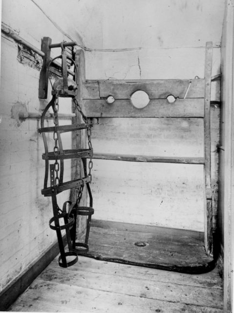 A gibbet cage with a skull in it stands in front of a wooden head rack