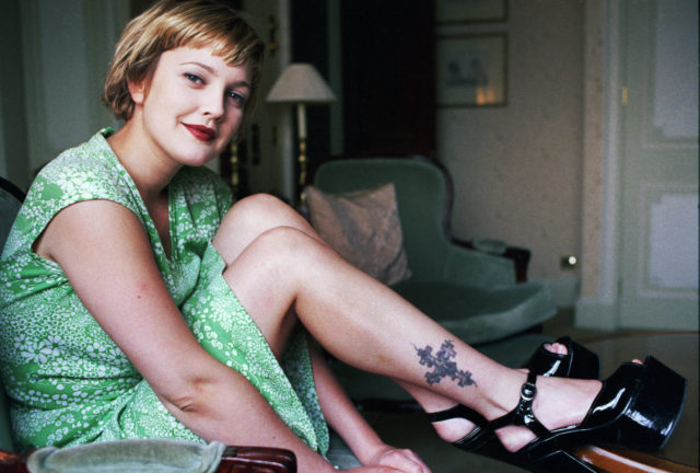 Drew Barrymore in a green dress with short hair, her ankle tattoo visible