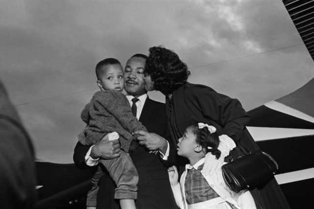 Martin Luther King Jr. with his wife kissing his cheek, holding his son, his daughter beside Coretta
