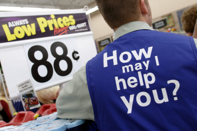 A man's back turned to the camera showing the Walmart slogan on his vest, a price sign reading "88 cents" behind him