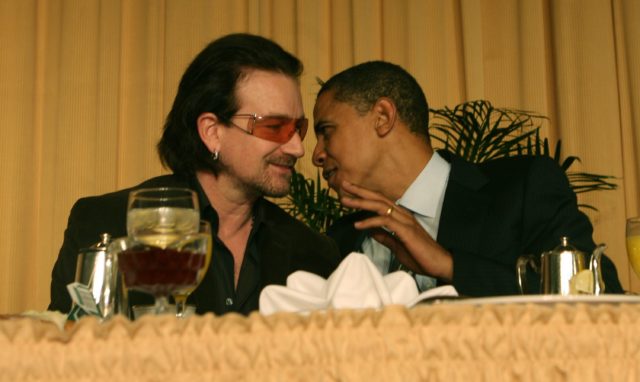 Barack Obama leaning in to speak to Bono at a table
