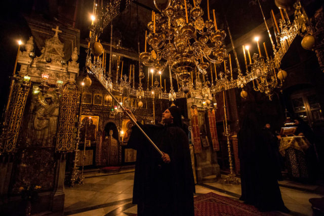 A monk lights candles in an ornate church