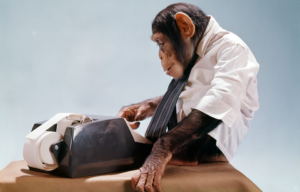 Chimpanzee sitting on a desk wearing a shirt and tie while typing at a typewriter.
