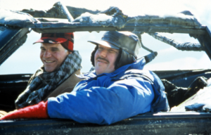 John Candy leaning out the window of a destroyed car, Steve Martin in the passenger seat, both wearing winter clothes