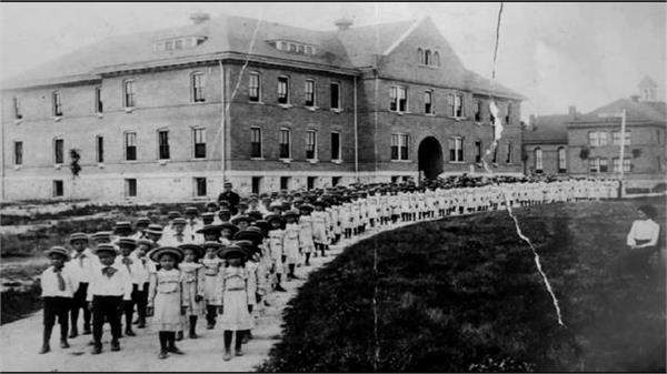 Rows of Native children in uniforms outside a boarding school building
