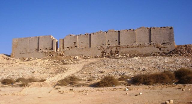 Temple wall ruins on a hill, the blue sky contrasting the sandy color of the walls