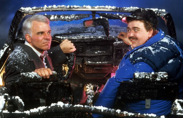 Steve Martin and John Candy looking at one another in a snow covered, destroyed car from "Planes, Trains and Automobiles"