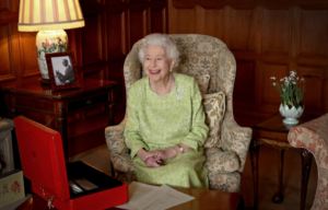 Queen Elizabeth in a green dress smiles brightly while sitting in a tall back chair.