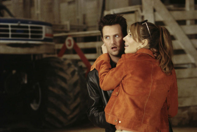 Elizabeth Hurley in an orange jacket with her arms around Matthew Perry, wearing a leather jacket in 'Serving Sara.'