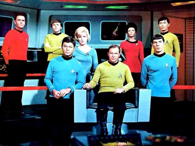 Group photo of the cast of 'Star Trek' standing around William Shatner sitting in a chair.