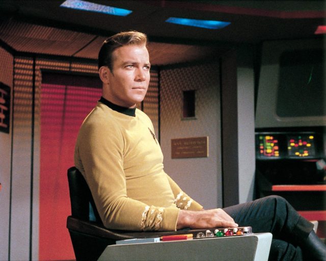 William Shatner as James T. Kirk on 'Star Trek' sitting in a chair on a space ship.