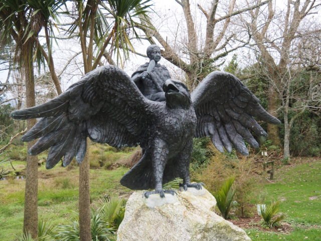 Life sized statue of a haast's eagle with a person holding a feather standing behind it.