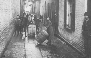 ull-length image of children standing with barrels in an alley strewn with clotheslines at a tenement building