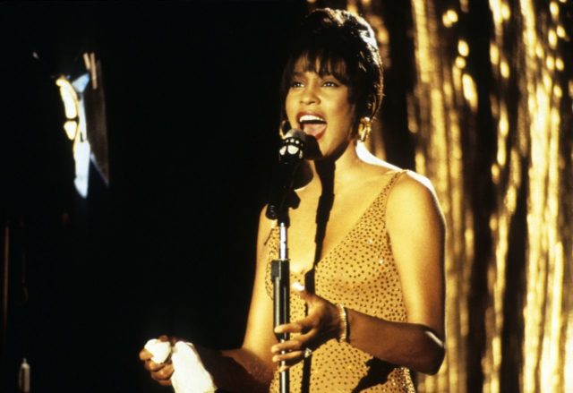 Whitney Houston in a bedazzled dress singing at a microphone