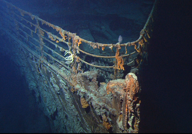 Bow of the Titanic underwater which is very rusty, but the metal railing remains intact.