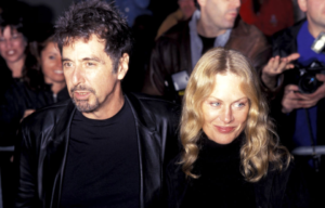 Al Pacino in a black shirt and jacket stands with his arm around Beverly D'Angelo, also in a black shirt.
