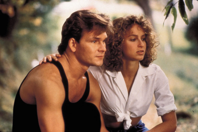Jennifer Grey as Baby Houseman in a white shirt with her arm around Patrick Swayze as Johnny Castle in a black tank top.
