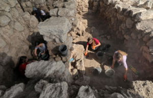 Group of people excavate a rock structure in the ground.