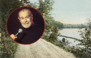 Headshot of George Carlin holding a microphone, on top of an image of a road with a body of water to the left