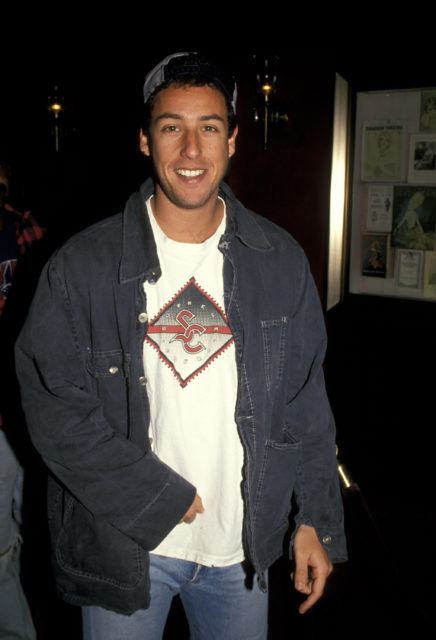 Headshot of Adam Sandler wearing a overshirt, t-shirt, and baseball cap
