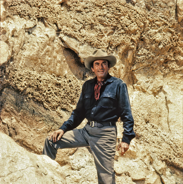 Gregory Peck in a cowboy outfit with his leg up on a rock.