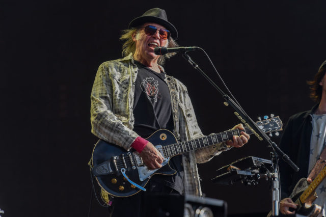 Neil Young singing into a microphone and playing the guitar.