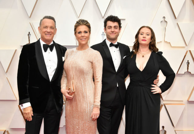 Tom Hanks in a black suit, Rita Wilson in a long pink dress, Truman Hanks in a black suit, and Elizabeth Hanks in a black dress, pose together on the red carpet.