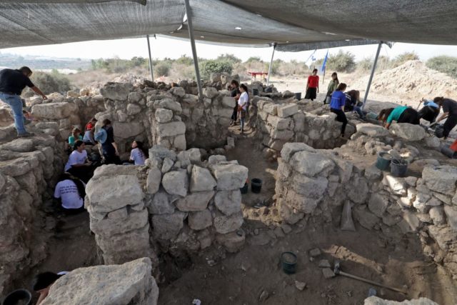 Group of people excavate the ground around stone walls under a tent.