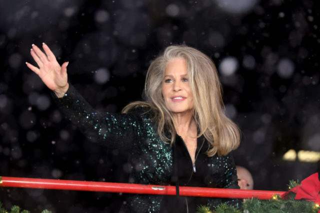 Beverly D'Angelo waves while wearing a sparkling jacket.