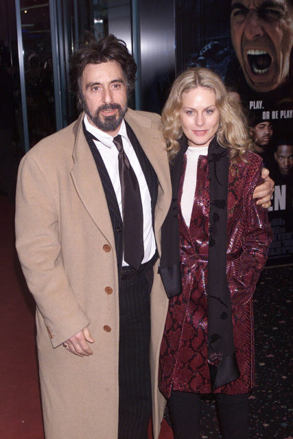 Al Pacino in a brown trench coat with his arm around Beverly D'Angelo in a pink snake skin coat.