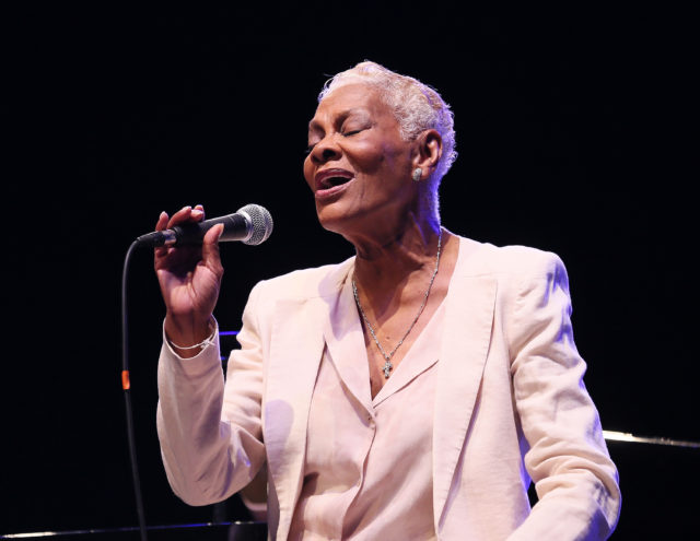 Dionne Warwick singing into a microphone eyes closed