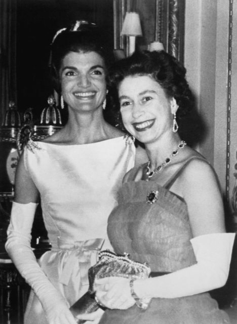 Headshot of Queen Elizabeth II standing in front of Jackie Kennedy in fancy dress