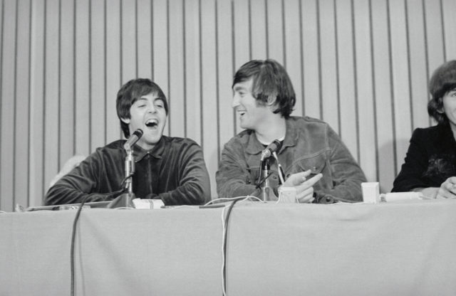 Paul McCartney and John Lennon laughing while sitting at a panel