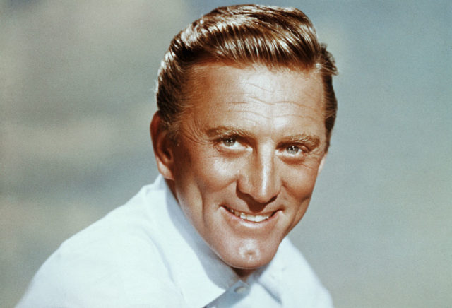 Headshot of Kirk Douglas in a white collared shirt smiling broadly at the camera.