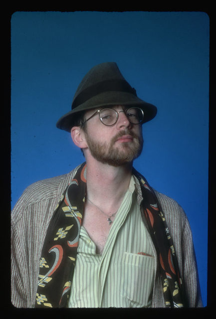 Michael O'Donoghue in a green striped shirt, fedora, and glasses.